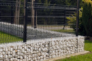 Çelik bir çitin altında alçak bir temel. Gabion.