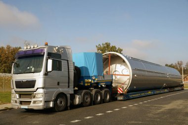 Uzun bir araç. Gümüş bir kamyon, düşük yükleme yarı römork ve büyük boy yük..