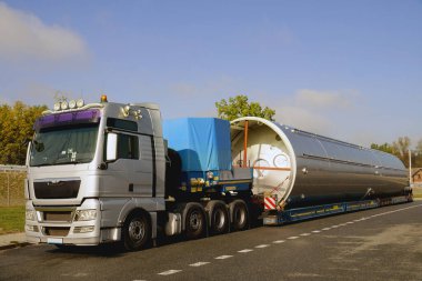 Gümüş bir kamyonet, düşük yüklenmiş yarı karavan ve büyük bir yük. Uzun araç.