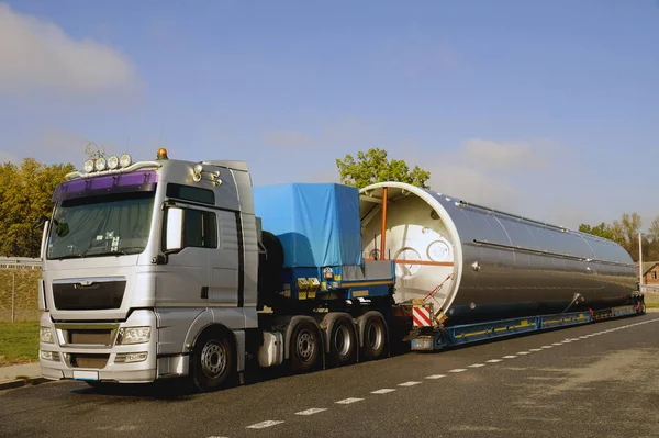 Gümüş bir kamyonet, düşük yüklenmiş yarı karavan ve büyük bir yük. Uzun araç.