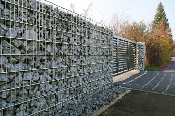 Fence made of gabions. Automatic gate controlled by a remote control in the wall.