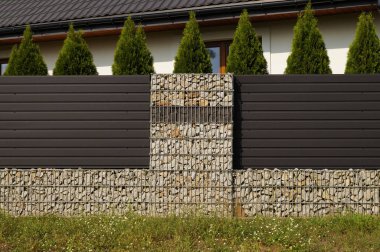 Ev, diğerleri arasında çelik sepetlere yerleştirilmiş taşlardan yapılmış bir çitle çevrilidir. Gabion.