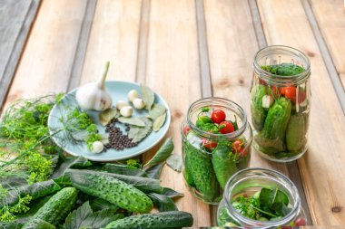 Tahta bir masada ve cam kavanozlarda dereotu, sarımsak ve baharatla konserve ve turşu yapmaya hazır taze salatalıklar.