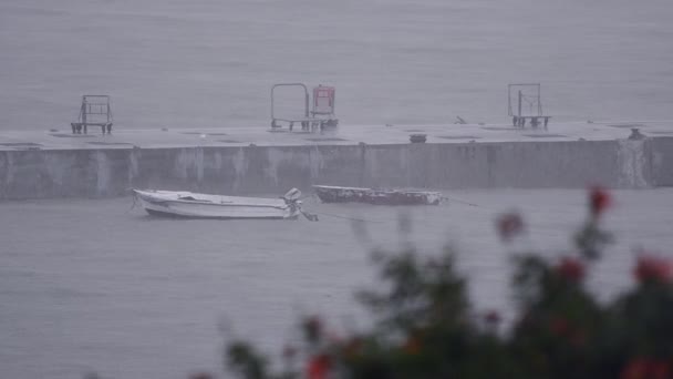 Dois pequenos barcos de pesca de madeira ancorados no cais com chuva pesada e mares tempestuosos — Vídeo de Stock