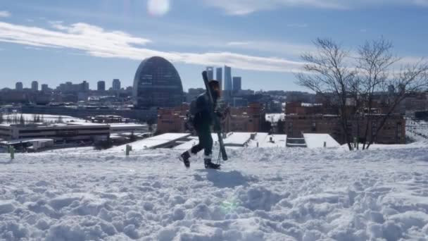 Een vrouw met ski 's loopt op sneeuw met uitzicht op de financiële district wolkenkrabbers in Madrid na een zware sneeuwval in Madrid, Spanje — Stockvideo