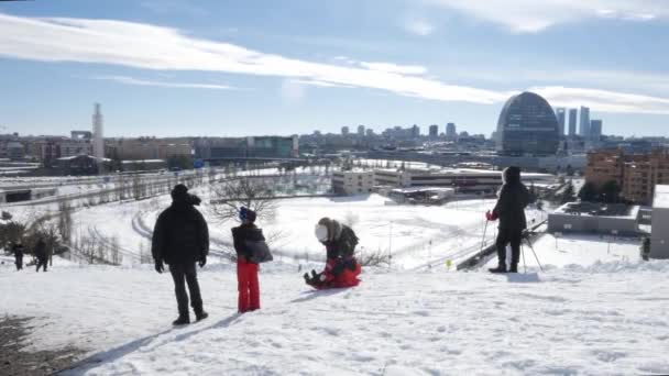 在西班牙马德里一场大雪之后，孩子们在冬日滑行。背景城市景观，包括Cuatro Torres区 — 图库视频影像