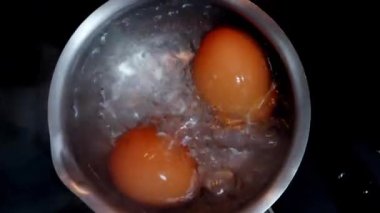 İki taze tavuk yumurtası paslanmaz çelik tavada kaynıyor, yakın plan, üst manzara.