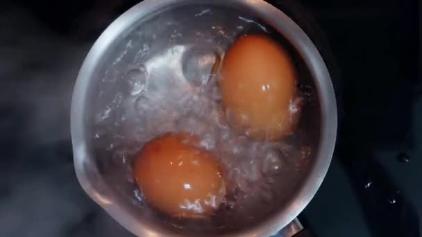 Два свежих куриных яйца, кипящих в кастрюле из нержавеющей стали, закрыть, вид сверху — стоковое видео