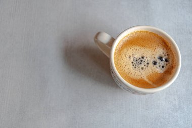 Sabah ışığında seramik gri bir yüzeyde iştah açıcı bir köpükle bir fincan kahve..