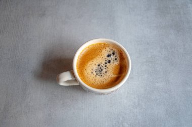 Sabah ışığında seramik gri bir yüzeyde iştah açıcı bir köpükle bir fincan kahve..