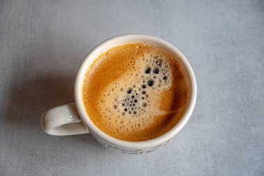 Sabah ışığında seramik gri bir yüzeyde iştah açıcı bir köpükle bir fincan kahve..