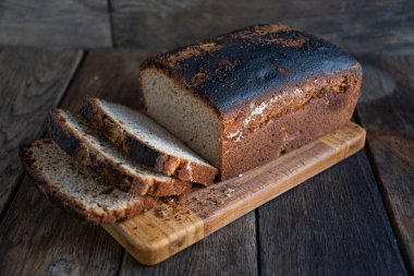 Sliced homemade bread lies on a kitchen board, on a wooden background.