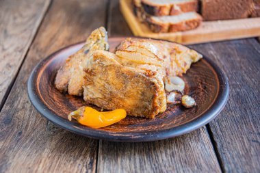 Fried fish with onions, yellow pickled peppers in a ceramic plate on a wooden background.