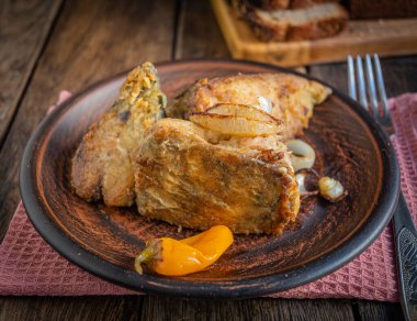 Fried fish with onions, yellow pickled peppers. Kitchen napkin and fork.