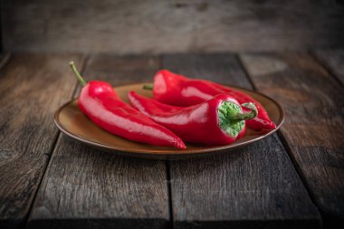  Üç iştah açıcı kırmızı biber seramik tabakta, ahşap mutfak masasında..