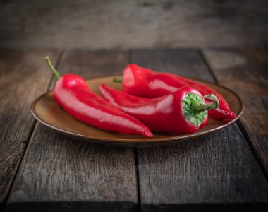  Üç iştah açıcı kırmızı biber seramik tabakta, ahşap mutfak masasında..