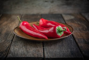  Üç iştah açıcı kırmızı biber seramik tabakta, ahşap mutfak masasında..