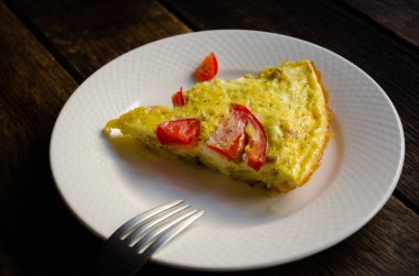 Beyaz tabakta kırsal bir omlet, ekmek, ahşap bir masada mutfak peçetesi..