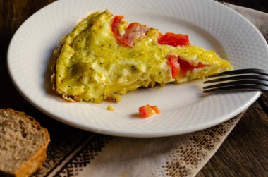 Beyaz tabakta kırsal bir omlet, ekmek, ahşap bir masada mutfak peçetesi..