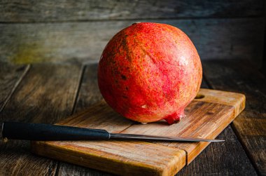 Mutfak tahtasındaki kırmızı nar ve bıçak. Olgun sağlıklı meyve. Mutfakta yemek pişirmek..