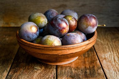 Tahta bir masada seramik bir kasede taze erik hasadı..