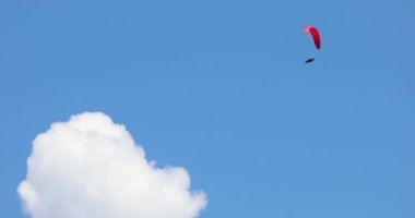 Mavi gökyüzünde kırmızı bir paraglider beyaz bir bulutun üzerinde uçuyor.