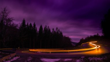 Akşamları asfalt bir yolda araba ışığı çizgileri, ağaçlar, bulutlu gökyüzü. Jeseniky Dağları, Çek Cumhuriyeti.