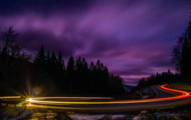 Akşamları asfalt bir yolda araba ışığı çizgileri, ağaçlar, bulutlu gökyüzü. Jeseniky Dağları, Çek Cumhuriyeti.