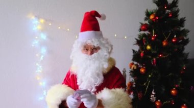 Beyaz sakallı yaşlı Noel Baba çocukları ve yetişkinleri kutluyor, elinde banknotlar tutuyor, onlara para veriyor, Noel konseptine odaklanıyor, tatil indirimleri, alışveriş, hediyeler.