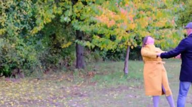 Sonbahar parkında ağaçların arka planında dans eden yaşlı adam ve kadın. Sağlıklı yaşam tarzı, iyi ruh hali, her yaşta mutluluk.