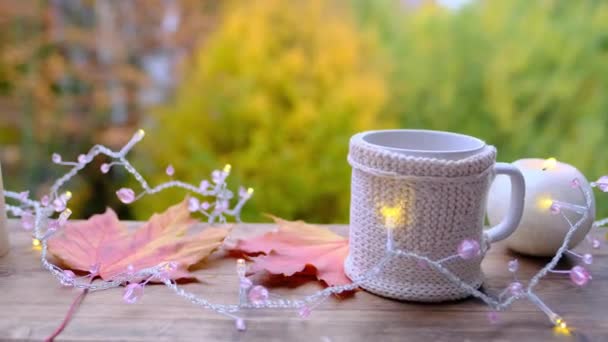 飲み物 マグカップのコーヒー 庭の木製テーブルの上のキャンドル 背景の美しいぼやけた自然の風景 天気の良いコンセプト 屋外ティーパーティー 居心地の良い秋の気分 — ストック動画