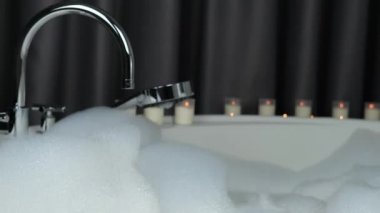 Kadın büyük yuvarlak bir banyoda oturur, ayaklarını köpükle yıkar, mumlar romantik bir şekilde yanar, iyi ruh hali konsepti, iş gününden sonra şehvetli bir rahatlama.