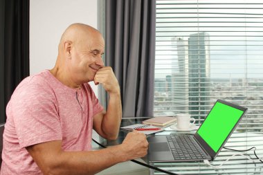 Adam bir dizüstü bilgisayarın arkasında çalışıyor. Modern Avrupa şehrinin penceresinin önündeki bir ofiste boş ekranla. İş fikirleri konsepti, işyeri.