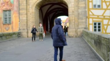 Bir Avrupa şehrinin sokaklarında ceketli ve beyaz maskeli genç bir adam yürüyor, iş seyahati, seyahat, covid-19 Coronavirus salgını dönemi
