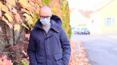 Ceketli ve beyaz maskeli genç adam bir Avrupa şehrinin sokaklarında yürüyor, iş gezisi konsepti, sonbaharda seyahat, covid-19 Coronavirus salgını dönemi