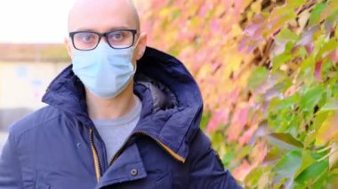 Ceketli ve beyaz maskeli genç adam bir Avrupa şehrinin sokaklarında yürüyor, iş gezisi konsepti, sonbaharda seyahat, covid-19 Coronavirus salgını dönemi