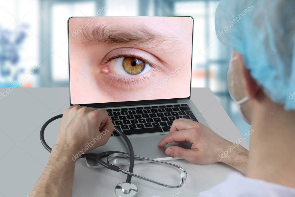 man, doctor, pharmacist in a white mask is sitting at a laptop, on the screen of human eyes close-up, concept of gadgets, modern technology in medicine, online consultation