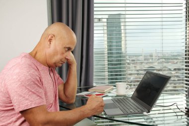 Adam bir dizüstü bilgisayarın arkasında çalışıyor. Modern Avrupa şehrinin penceresinin önündeki bir ofiste boş ekranla. İş fikirleri konsepti, işyeri.