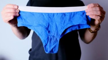 Elinde mavi kadın donu tutan bir adam, örgü iç çamaşırı, rahat kıyafetler konsepti, kadın mahrem sorunları