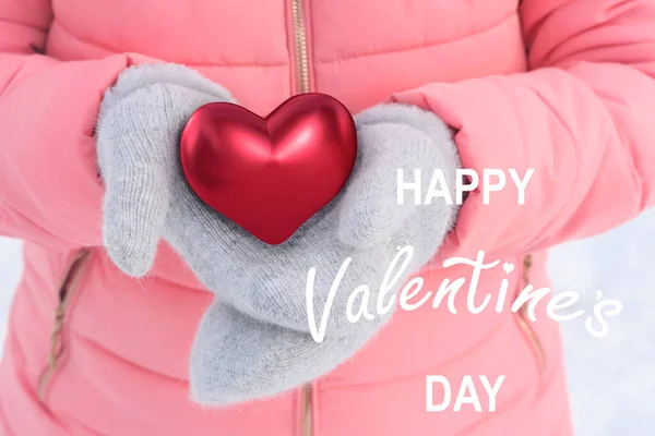 身穿粉色夹克的女孩 手持红心模特 象征爱情 手中拿着灰色羊毛手套 冬天的背景和白雪 忏悔的概念 情人节 — 图库照片