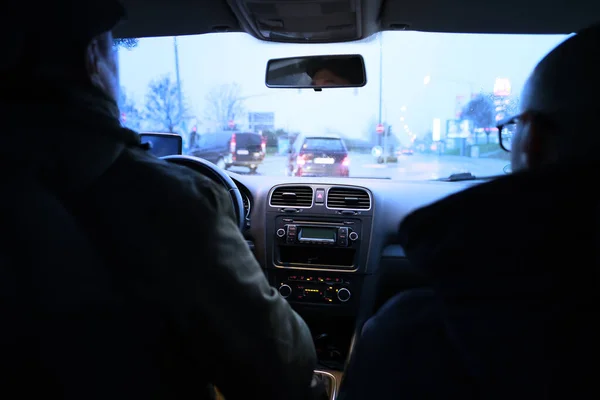 two men are driving a car in the evening in the rain along city streets, the concept of road traffic, traffic jams, traveling by personal transport