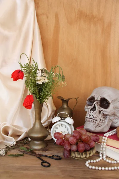 野の花古い真鍮のジャグの古い木製のテーブル 頭蓋骨 目覚まし時計 ブドウ シルクのドレープラリー 象徴的なオランダの静物画のコンセプト — ストック写真