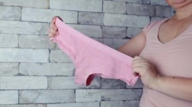 Elinde ipek pembe kadın külotu tutan kadın, örgü iç çamaşırı, rahat kıyafetler konsepti, kadın mahrem sorunları 