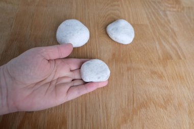 Düz beyaz taşlar doğal ahşap arka planda yatar, kadın eli bir objeyi tutar, arka plan boşluklu, spa prosedürleri konsepti, masaj, antik runik yazılar hakkında falcılık.