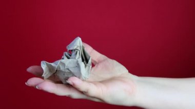 Kadın eli, kırmızı zemin üzerine buruşuk gri ambalaj kağıdı, gerginlik konsepti, psikolojik istismar, stres atma, yenilenebilir malzemelerin geri dönüşümü