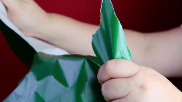 赤い背景に緑の紙を引き裂く女性の手 贈り物の包装 お祝い 再生可能な材料をリサイクルするという概念 — ストック動画