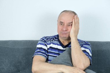 Yaşlı kel adam kanepede oturuyor, kafasını ellerinin arasına alıyor, yüzünde acı çekiyor, problem konsepti, stres, baş ağrısı, migren krizi