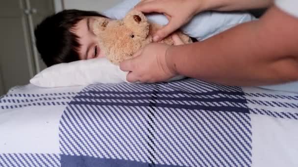 一个八岁的男孩躺在床上 用手轻轻地抱着一只泰迪熊 这是学童焦虑睡眠的概念 是失眠 是夜晚的恐惧 — 图库视频影像
