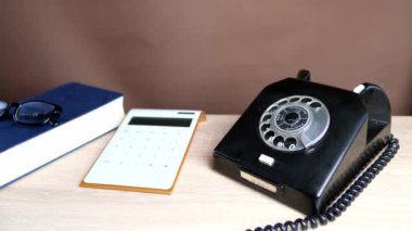 Siyah bir telefonun alıcısını tutan, yardım hattında konuşan, hesap makinesi, kahverengi arka plan, psikolojik destek kavramı, farklı yılların teknolojisi...