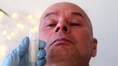 Yaşlı, kel bir adamın yüzü, laboratuvar asistanı, doktor burun mukozasından koronavirüs, DNA tespiti, COVID-19 konsepti için örnek alıyor.